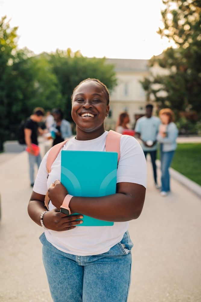 A smiling learner holding her books on campus